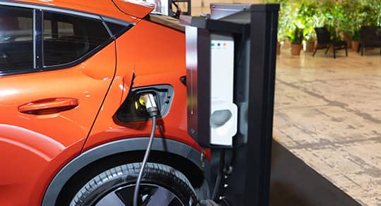 Gros plan d'une voiture électrique orange connectée à une borne de recharge