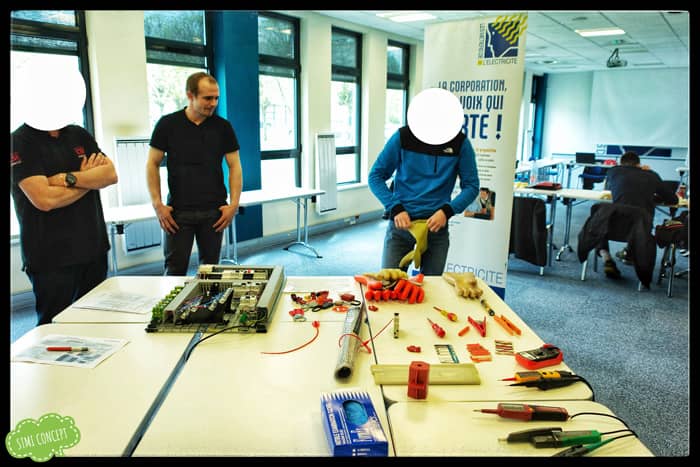 Plusieurs personnes se tiennent debout autour d'une table présentant des outils et du matériel électrique dans une salle de formation