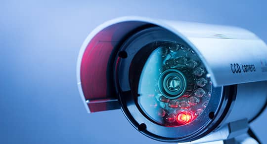 Gros plan d'une caméra de sécurité argentée avec boîtier de protection et voyant lumineux rouge.